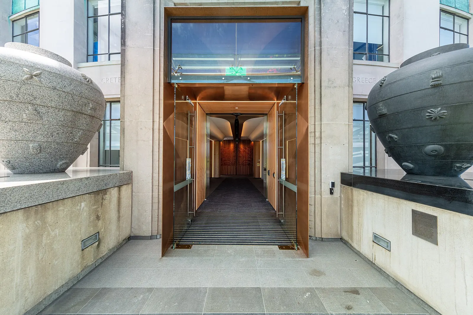 Ein Türdurchgang des Auckland Museum in kupferfarbenem Metall gefasst, mit je einem großen geschnitzten Steingefäß zu beiden Seiten