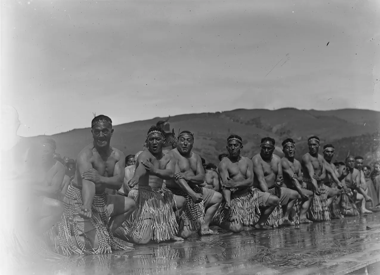 Eine Reihe von Männern in traditioneller Kleidung, die vor Hügeln knien, eine Kulturvorführungsgruppe, fotografiert in den 1940er Jahren